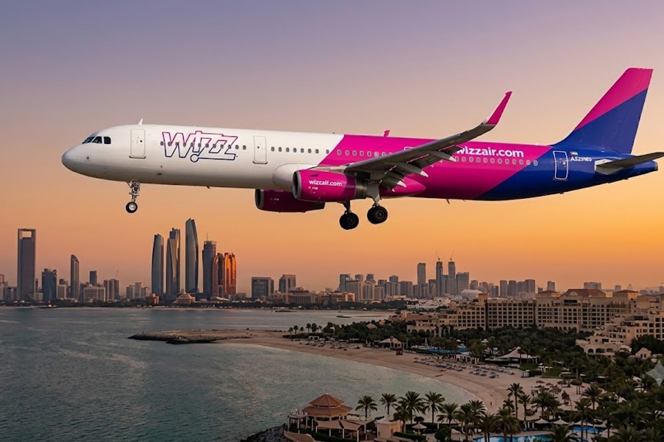 Commercial jetliner flying over desert sands toward modern Arabian Gulf cityscape during winter sunset