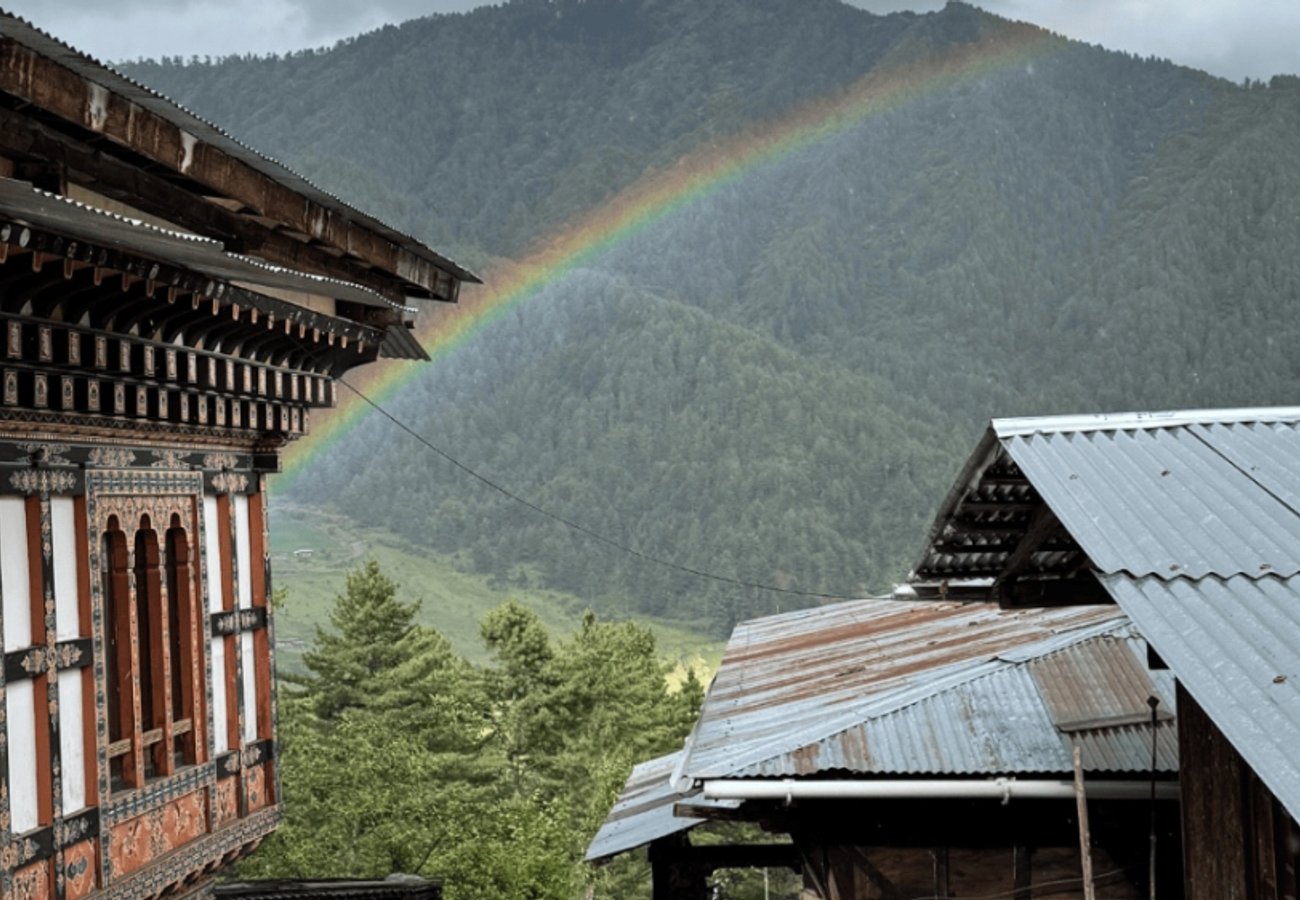 Rainbow appearing over traditional carved wooden Bhutanese house and green mountain valley