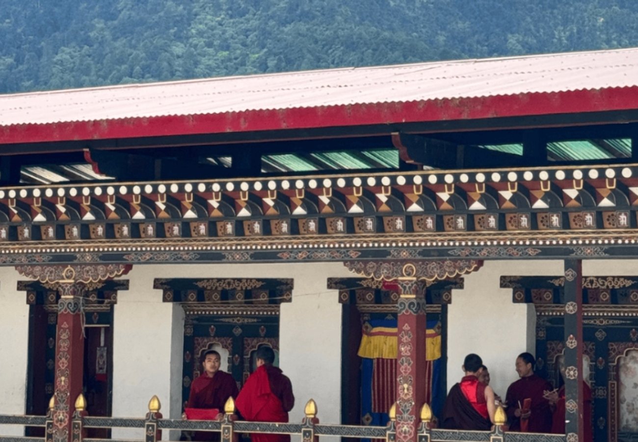 Buddhist monks in red robes conversing in a traditional decorated Bhutanese monastery courtyard
