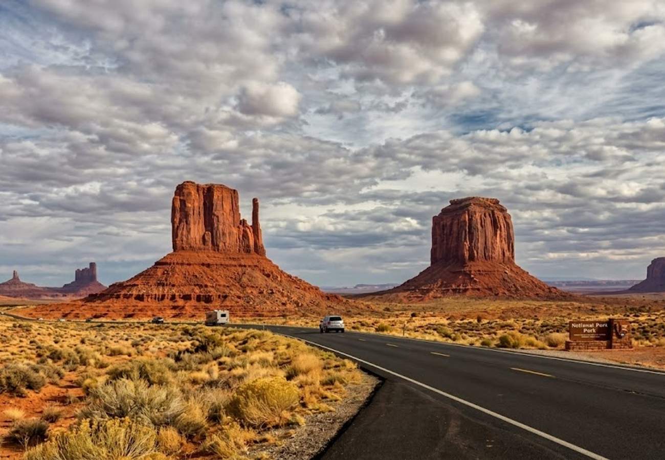 Iconic twin red sandstone mittens rising from a flat desert plain along a scenic highway with dramatic cloud formations