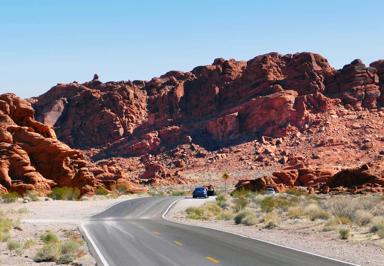 Paved scenic highway winding through glowing fiery red Aztec sandstone rock formations in Valley of Fire State Park