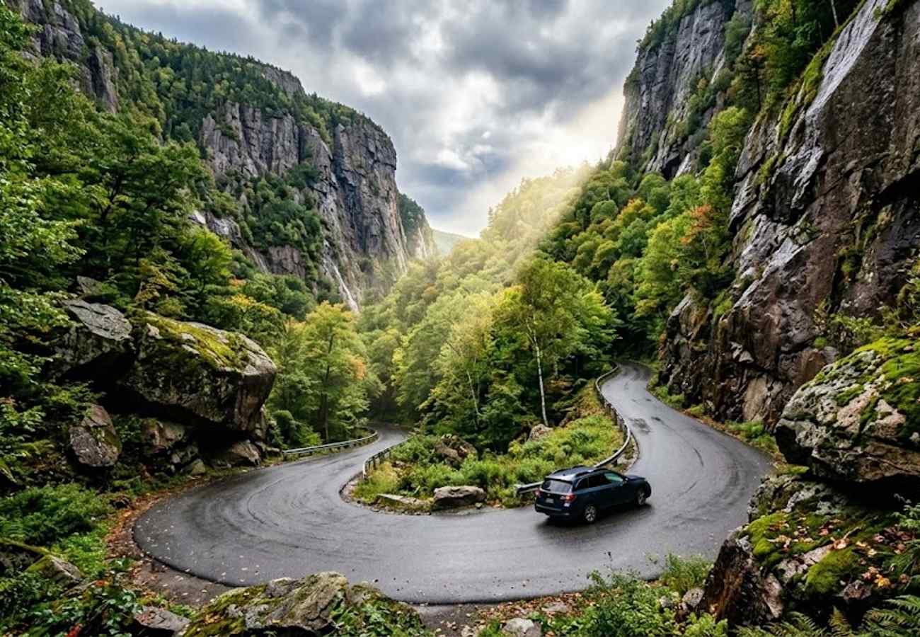 Paved mountain road twisting tightly between towering mossy granite cliffs and massive boulders in Smugglers Notch Vermont