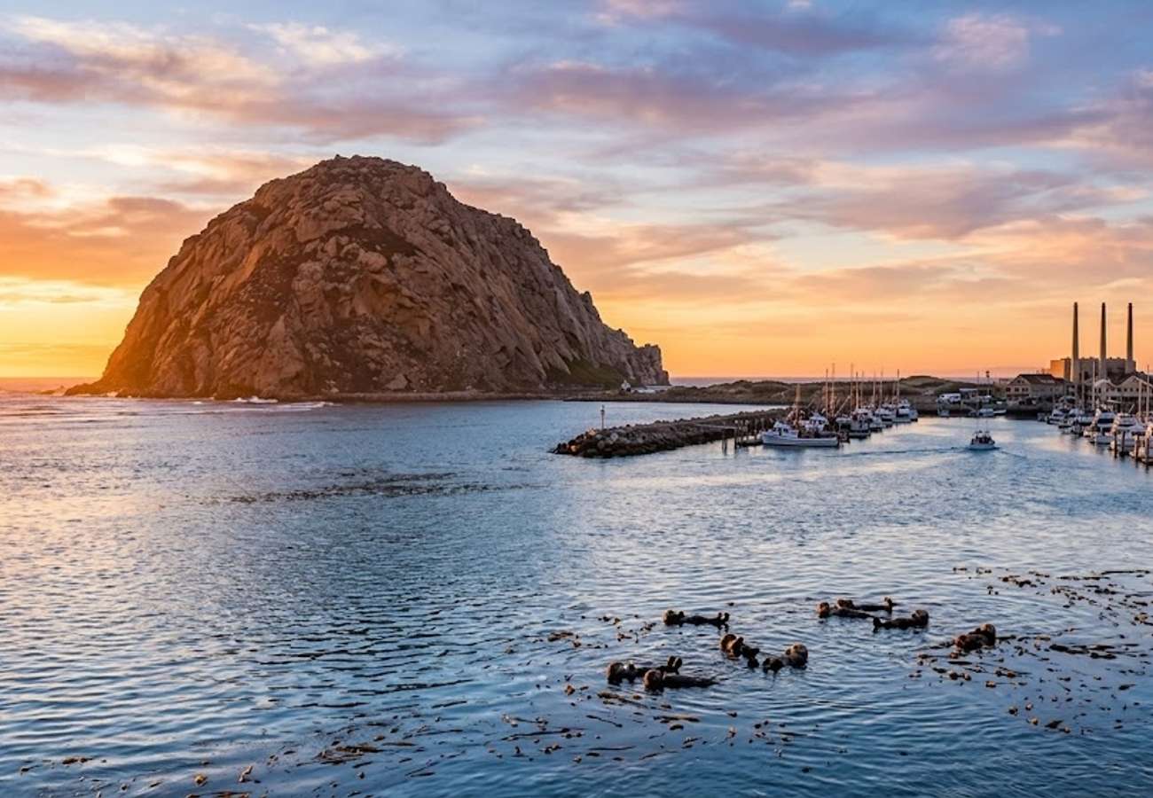 Massive 576-foot volcanic Morro Rock monolith rising from the ocean at harbor mouth with calm waters and blue sky in California