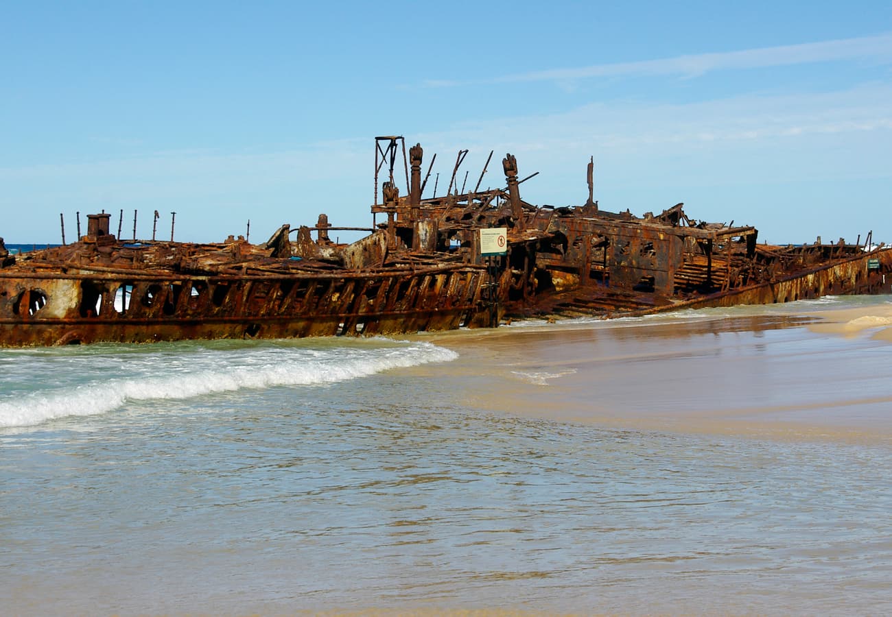 The historic rusted hull of the SS Maheno shipwreck stranded on the sand of K'gari