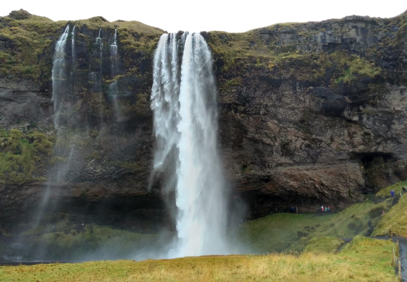 Travelers walking the wet pathway behind the falling veil of Seljalandsfoss