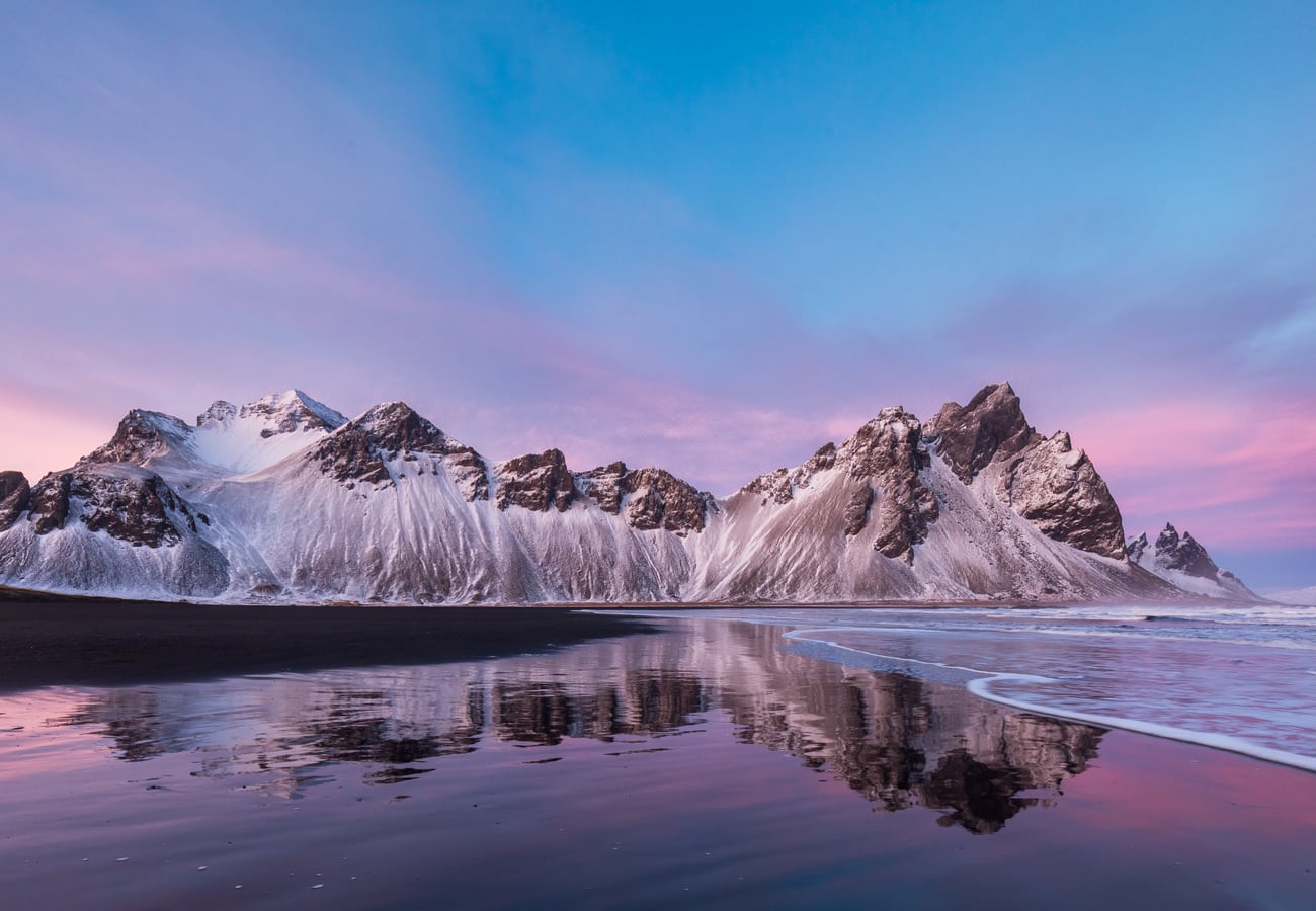 Jagged peaks of Vestrahorn mountain reflected in wet black sand at sunset