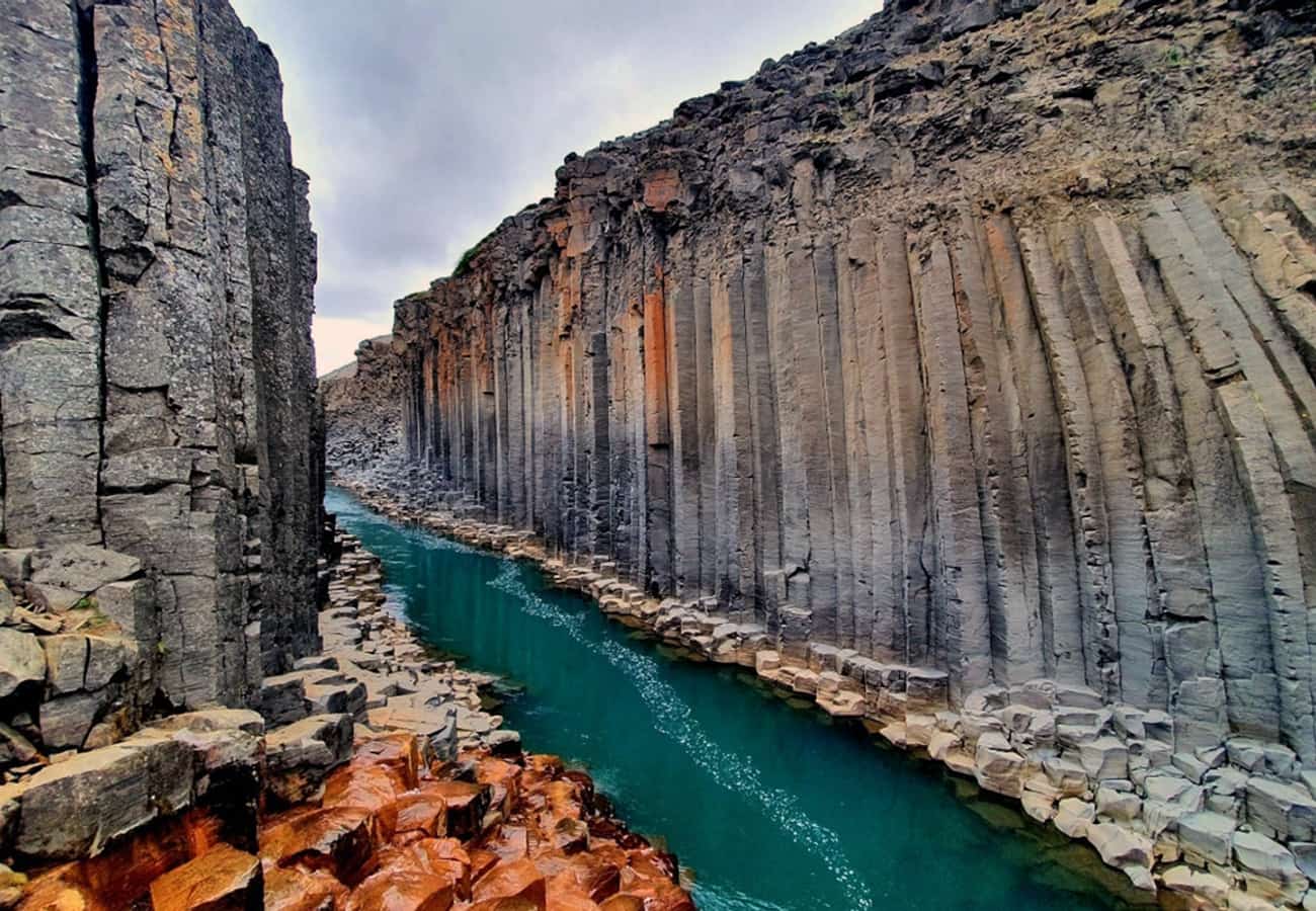 Colossal vertical basalt columns flanking the turquoise river of Stuðlagil Canyon