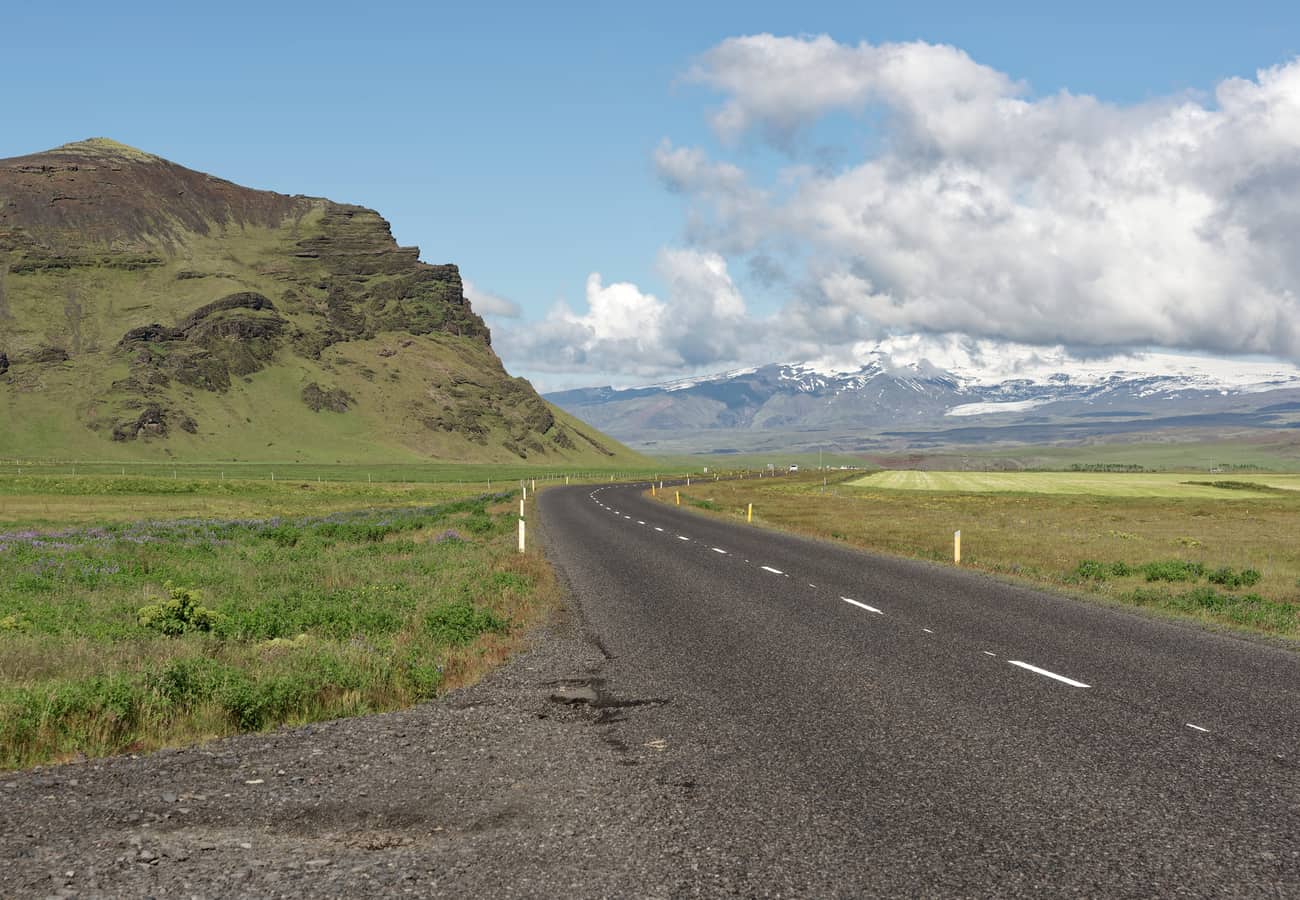 Paved asphalt of Route 1 cutting through green volcanic plains in South Iceland