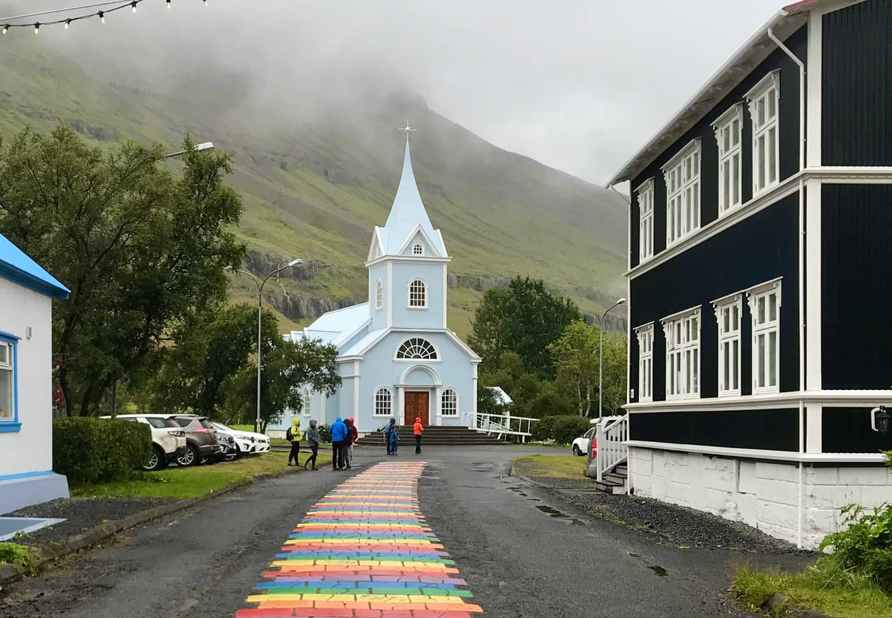 Historic pale blue wooden church and rainbow street in the fjord town of Seyðisfjörður