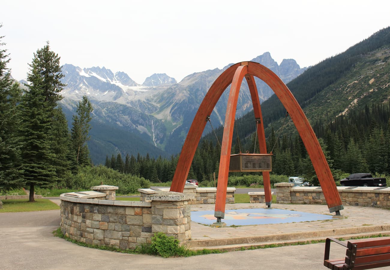 The Rogers Pass Summit Monument standing beneath massive glaciated mountain walls along the Trans-Canada Highway